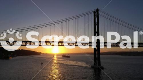 Silhouette Of Ponte 25 De Abril Suspension Bridge At Sunset And Sailing Yacht. 25th April Bridge. Portugal. Golden Hour. Aerial View. Drone